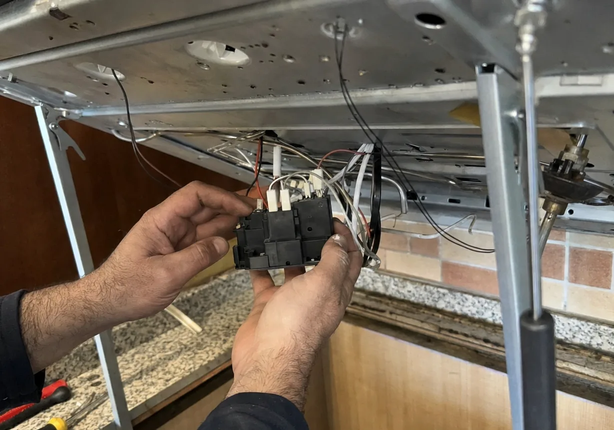 A cooking appliance lifted out of its worktop cutout on supports, its loom and terminal block held clear so the connections can be read